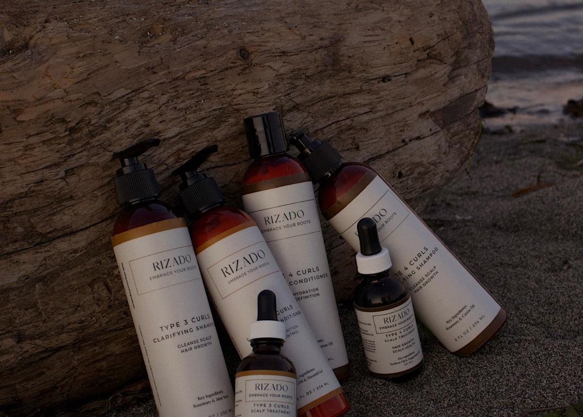 Collection of Rizado hair care products on a beach with a wooden log.